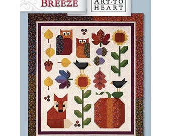May include: A quilt titled Autumn Breeze by Art to Heart featuring a cream center panel with appliqued motifs of owls, a fox, sunflowers, pumpkins, acorns, and autumn leaves in shades of orange, brown, yellow, and green with a dark floral border.