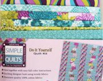 May include: A Simple Quilts Do It Yourself Quilt Kit featuring stacked fabric strips in shades of purple, teal, lime green, and white. The packaging displays the finished quilt design, text, and dimensions of 44 inches by 53 inches for the project.