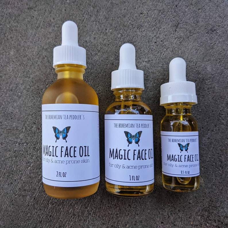 May include: Three amber glass bottles with white dropper tops and labels. The labels are white with black text and a blue butterfly graphic. The text on the labels reads "The Bohemian Tea Peddler's Magic Face Oil" and lists the size of the bottle in fluid ounces. The bottles are arranged in order of size from left to right.