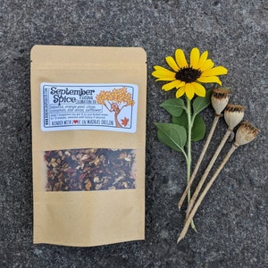 May include: A kraft paper bag of "September Spice" tea with a clear window, a yellow sunflower, and three dried seed pods. The tea label lists ingredients: hibiscus, orange peel, clove, cinnamon, star anise, and safflower.