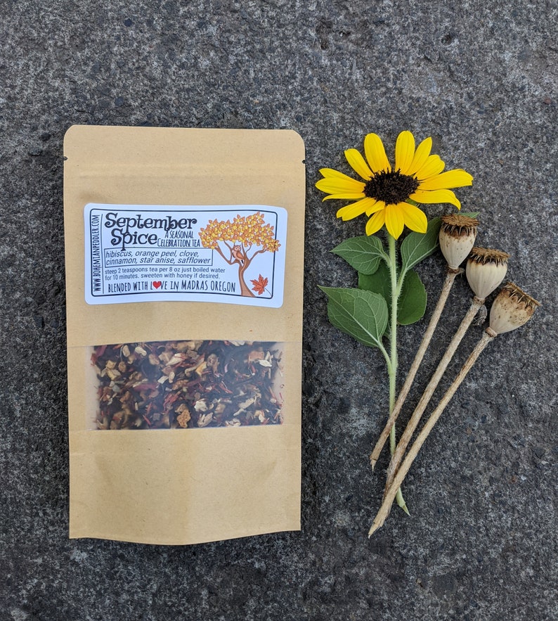 May include: A kraft paper bag of "September Spice" tea with a clear window, a yellow sunflower, and three dried seed pods. The tea label lists ingredients: hibiscus, orange peel, clove, cinnamon, star anise, and safflower.