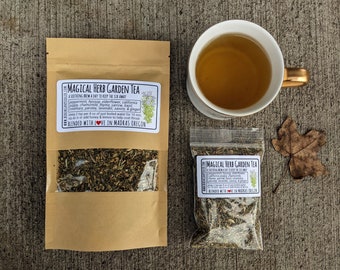 May include: Two bags of Magical Herb Garden Tea, a soothing brew to keep the ick away. The tea blend includes peppermint, hyssop, elderflower, California poppy, chamomile, thyme, yarrow, bank rosemary, parsley, lavender, savory, and ginger. The tea is blended with love in Madras, Oregon. A cup of the tea is shown in a white mug with a gold handle.