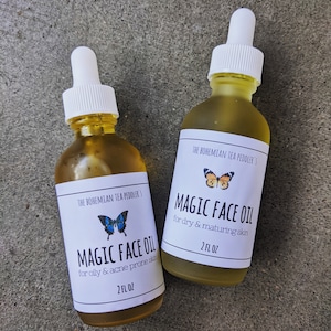 May include: Two glass bottles of face oil with white labels and butterfly illustrations. The labels read "The Bohemian Tea Peddler's Magic Face Oil" and specify the oil's use for either oily or dry skin. Each bottle contains 2 fl oz.