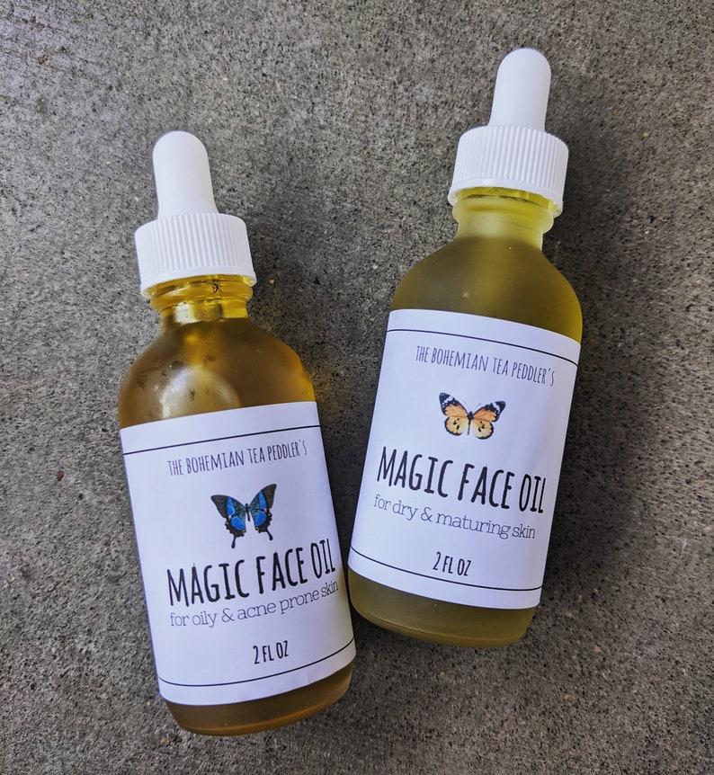 May include: Two glass bottles of face oil with white labels and butterfly illustrations. The labels read "The Bohemian Tea Peddler's Magic Face Oil" and specify the oil's use for either oily or dry skin. Each bottle contains 2 fl oz.