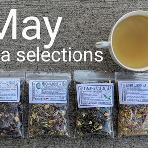 May include: Four small bags of loose leaf tea with labels that read "Bellflower Blend", "Moon Goddess Tea", "Jasmine Green Tea", and "Flower Garden Tea". The tea blends are visible in the bags. The bags are arranged in a row on a gray surface. The text "May tea selections" is written in white letters on a gray background above the bags.