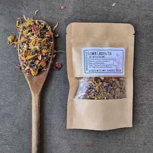 May include: A brown paper pouch with a clear window showing a blend of dried flowers and herbs. The pouch has a white label with the text "FLOWER GARDEN TEA" and instructions for brewing the tea. The text "BLENDED WITH LOVE IN MADRAS OREGON" is also on the label.