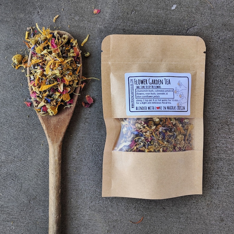 May include: A brown paper pouch with a clear window showing a blend of dried flowers and herbs. The pouch has a white label with the text "FLOWER GARDEN TEA" and instructions for brewing the tea. The text "BLENDED WITH LOVE IN MADRAS OREGON" is also on the label.