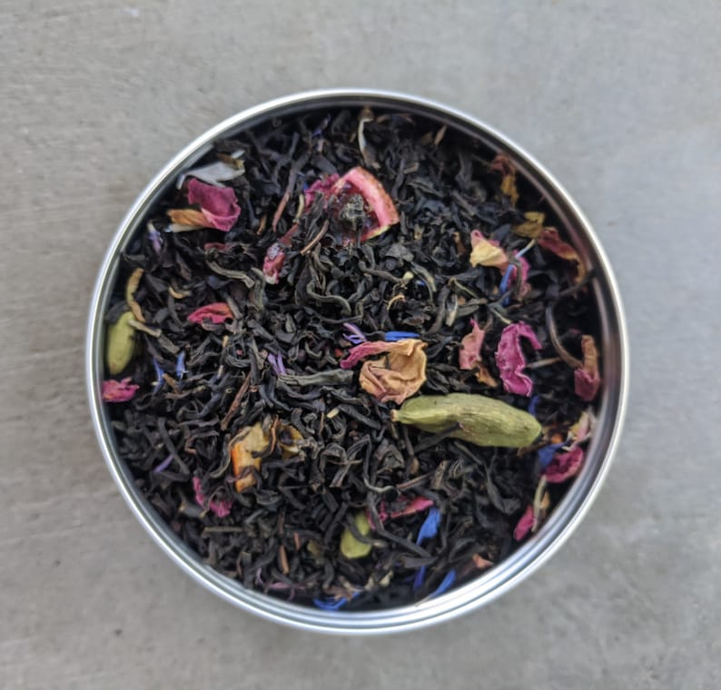 Puede incluir: Primer plano de una lata de metal llena de hojas de t&eacute; negro, p&eacute;talos de rosa secos y otros ingredientes florales.