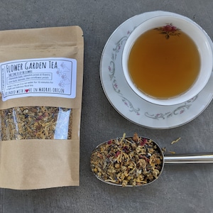 May include: A brown paper bag with a clear window showing a blend of dried flowers and herbs. The bag is labeled "Flower Garden Tea" and includes instructions for brewing the tea. The tea is blended with love in Madras, Oregon.