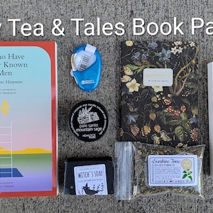 May include: A collection of items including a book titled "I Who Have Never Known Men", a floral-patterned notebook, a blue tape dispenser, a candle, soap, tea, and a pen set. The text "May Tea & Tales Book Pack" is at the top.