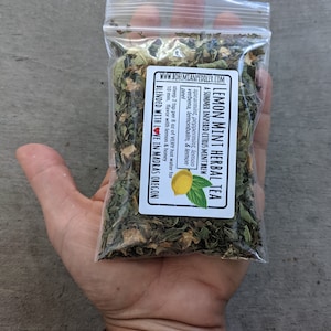 May include: A clear plastic bag filled with a blend of dried herbs for making lemon mint herbal tea. The bag is labeled "Lemon Mint Herbal Tea" and lists the ingredients: spearmint, peppermint, lemon verbena, lemon balm, and lemon peel. The label also includes instructions for steeping the tea and a note that it is blended with love in Madras, Oregon.