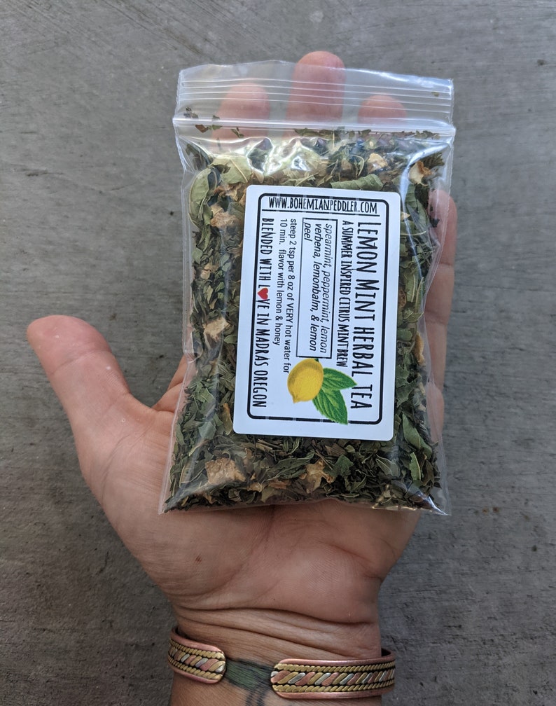 May include: A clear plastic bag filled with a blend of dried herbs for making lemon mint herbal tea. The bag is labeled "Lemon Mint Herbal Tea" and lists the ingredients: spearmint, peppermint, lemon verbena, lemon balm, and lemon peel. The label also includes instructions for steeping the tea and a note that it is blended with love in Madras, Oregon.