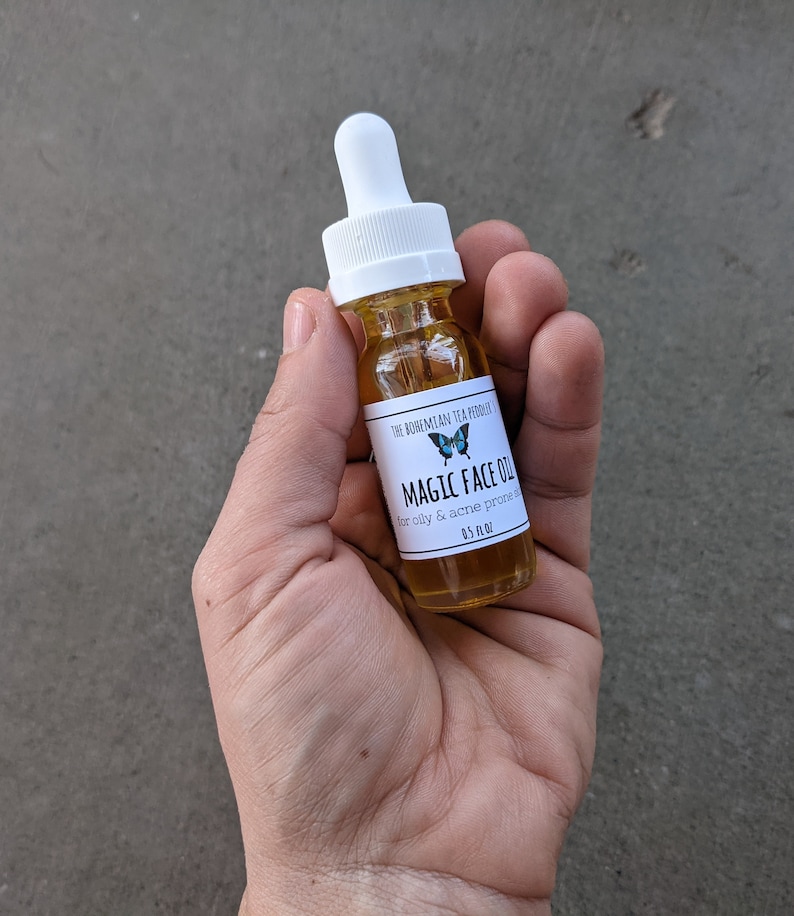 May include: A small glass bottle with a white dropper top and a white label. The label has a blue butterfly graphic and the text "The Bohemian Tea Producer Magic Face Oil for oily & acne prone skin 0.5 fl oz".
