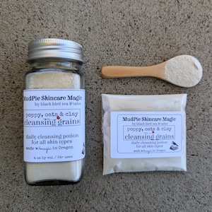 May include: A glass jar and a small packet of cleansing grains, with a wooden spoon. The jar and packet have labels that read "MudPie Skincare Magic" and "poppy, oats & clay cleansing grains". The labels also state the product is a daily cleansing potion for all skin types.