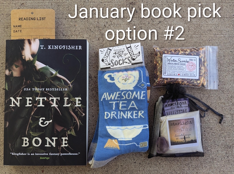May include: A gift set including a book by T. Kingfisher, socks with "Awesome Tea Drinker" text, tea, and a bag with "starlight" text. The set is labelled "January book pick option #2". The book is titled "Nettle & Bone".