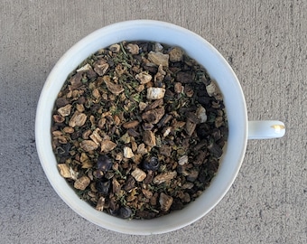 May include: A white ceramic bowl filled with a blend of dried herbs and berries for tea. The blend includes dried ginger, juniper berries, and other herbs.