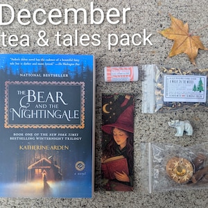 May include: A flat lay of a "December tea & tales pack" with a book, bookmark, tea, lip balm, incense, and a small bear figurine. The book is titled "The Bear and the Nightingale" by Katherine Arden.