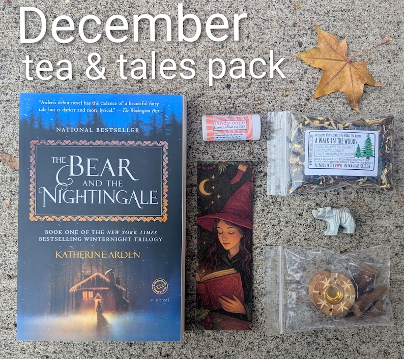 May include: A flat lay of a "December tea & tales pack" with a book, bookmark, tea, lip balm, incense, and a small bear figurine. The book is titled "The Bear and the Nightingale" by Katherine Arden.