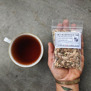 May include: A white pouch with a label that reads "White Willow Pain Relief Tisane A Traditional Pain Relief Decoction" and lists the ingredients as "white willow bark, cramp bark, ginger root". The label also includes instructions for brewing the tisane and states that it is "Blended with Love in Madras Oregon".