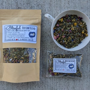 May include: A brown paper bag with a clear window showing a blend of dried herbs and flowers. The bag has a label that reads "Blissful Bedtime Blend" and includes a list of ingredients and instructions. The label also includes a small illustration of a sleeping person and a moon.