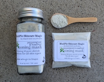 May include: A glass jar and a small packet of toning mask powder, with a wooden spoon holding some powder. The jar and packet have labels that read "MudPie Skincare Magic" and "peppermint & comfrey toning mask". The jar contains 4 oz of product.