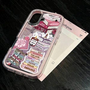 May include: Transparent phone case with a pink trim, adorned with book and rose stickers. The stickers feature text such as "Dark Romance," "Fantasy," and "Thriller." A pink card, styled like an Instagram post, is in the background.