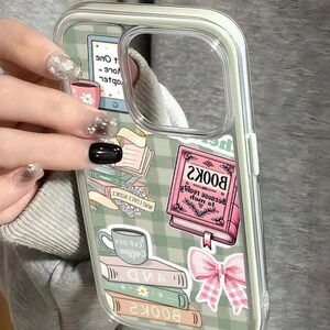May include: Clear phone case with a green and white checkered pattern. The case features book and coffee cup graphics, along with the text "BOOK2" and "COB OF". A pink bow and a stack of books are also visible.