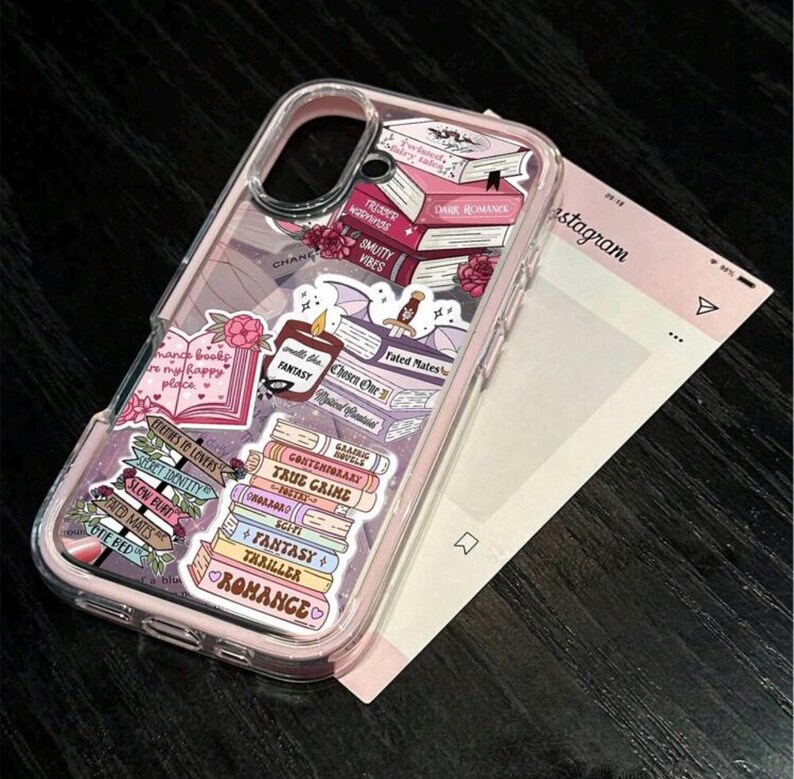 May include: Clear phone case with a pink border, decorated with stickers of books and text. The stickers include titles like "Dark Romance," "Fantasy," and "Thriller." The case also features floral accents and the Instagram logo.