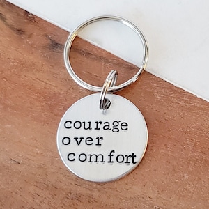 May include: Silver keychain with a round tag that reads "courage over comfort".