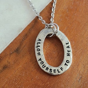 May include: Silver necklace with an oval pendant that reads "Allow yourself to heal".