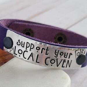 May include: Purple leather bracelet with a silver charm that says "Support Your Local Coven".