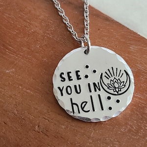 May include: Silver necklace with a round pendant that says "See you in hell" with a crescent moon and a lotus flower design.