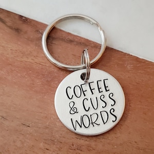 May include: Silver keychain with a round tag that says "Coffee & Cuss Words" in black lettering.