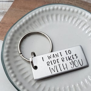 May include: Silver keychain with a rectangular tag that reads "I want to ride bikes with you".