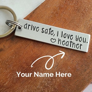 May include: Silver keychain with a metal tag that reads "drive safe, i love you. ♥ heather". The keychain is on a wooden surface.