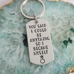 May include: Silver keychain with a tag that reads "You said I could be anything so I became myself" with a gender symbol.