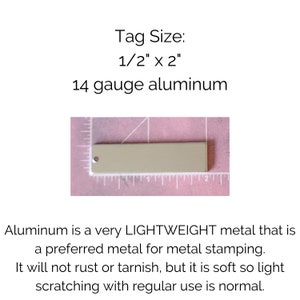 K&ouml;nnte beinhalten: Nahaufnahme einer 1,27 cm x 5,08 cm gro&szlig;en Aluminium-Etikette in St&auml;rke 14. Die Etikette ist hellgrau und hat oben ein Loch. Die Etikette liegt auf einer rosa Oberfl&auml;che mit einem Lineal dahinter.
