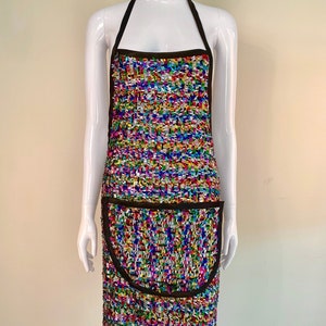 May include: A colorful, multi-colored apron with a black trim and a large pocket. The apron is made of a textured fabric and has a rainbow pattern.