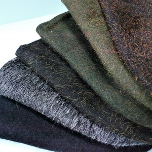 May include: A selection of textured fabric swatches in a range of colours. The fabrics include shades of black, grey, green, and brown, with visible fibres and a slightly fuzzy texture. The swatches are arranged in a fan, displaying their different colours and textures.