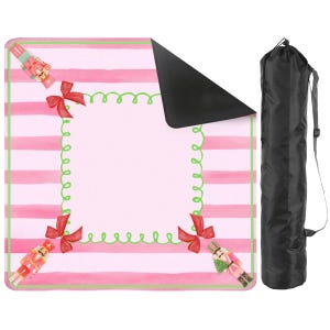 May include: A square blanket featuring a pink and white horizontal striped pattern with a central light pink square framed by a green squiggly border and red bows at the corners, accented by nutcracker figures, accompanied by a black carrying bag.