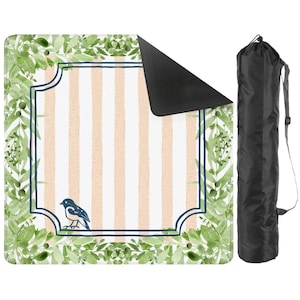 May include: A picnic blanket with a striped peach and white design, framed by green foliage and a navy border. A small blue bird is featured in the corner. Includes a black carrying bag.