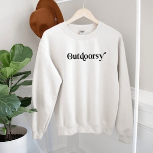 May include: A cream colored sweatshirt with the word "Outdoorsy" printed in black on the front.
