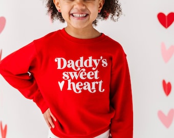 May include: A red sweatshirt with white text that says "Daddy's sweet heart" with a heart symbol. The sweatshirt is being worn by a young child.