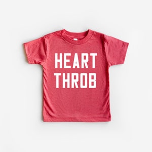 May include: Red short-sleeved t-shirt with the text "HEART THROB" in white.