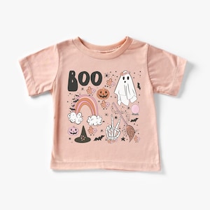 May include: A pink short-sleeved t-shirt with a graphic print of a ghost, rainbow, pumpkins, a witch's hat, a skeleton hand, a broom, and the word "BOO".