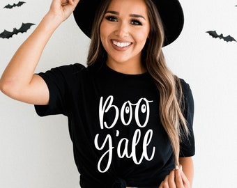 May include: A black t-shirt with the text "BOO y'all" in white lettering. The shirt is worn by a person with long brown hair and a black hat.