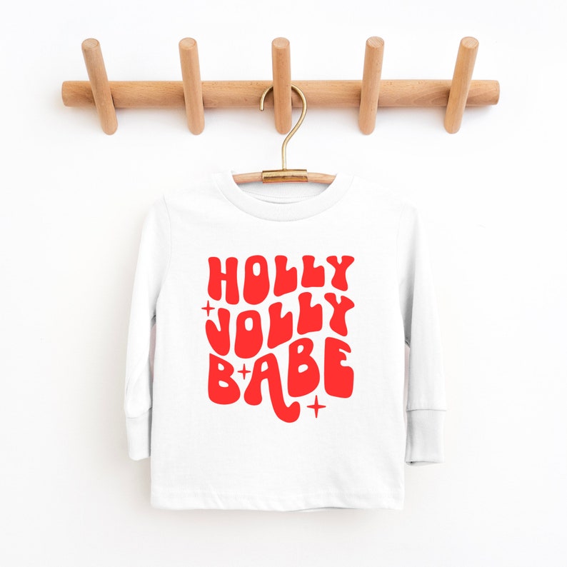May include: White long-sleeve shirt with a red graphic that says "HOLLY JOLLY BABE" in a retro font.
