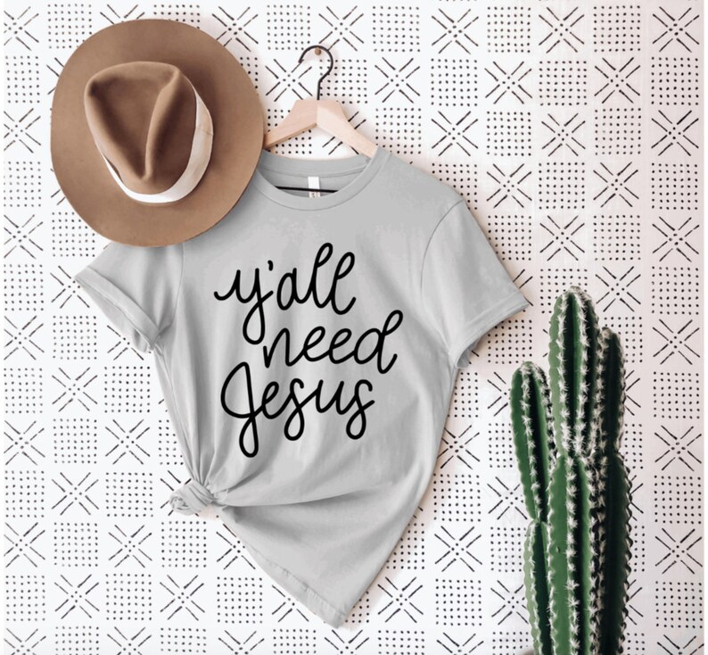 May include: A gray t-shirt with the text "y'all need Jesus" written in black cursive lettering.
