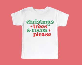May include: White t-shirt with green and red text that reads "christmas trees & cocoa please"