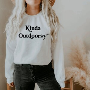 May include: White long-sleeve sweatshirt with the text "Kinda Outdoorsy" in black lettering.